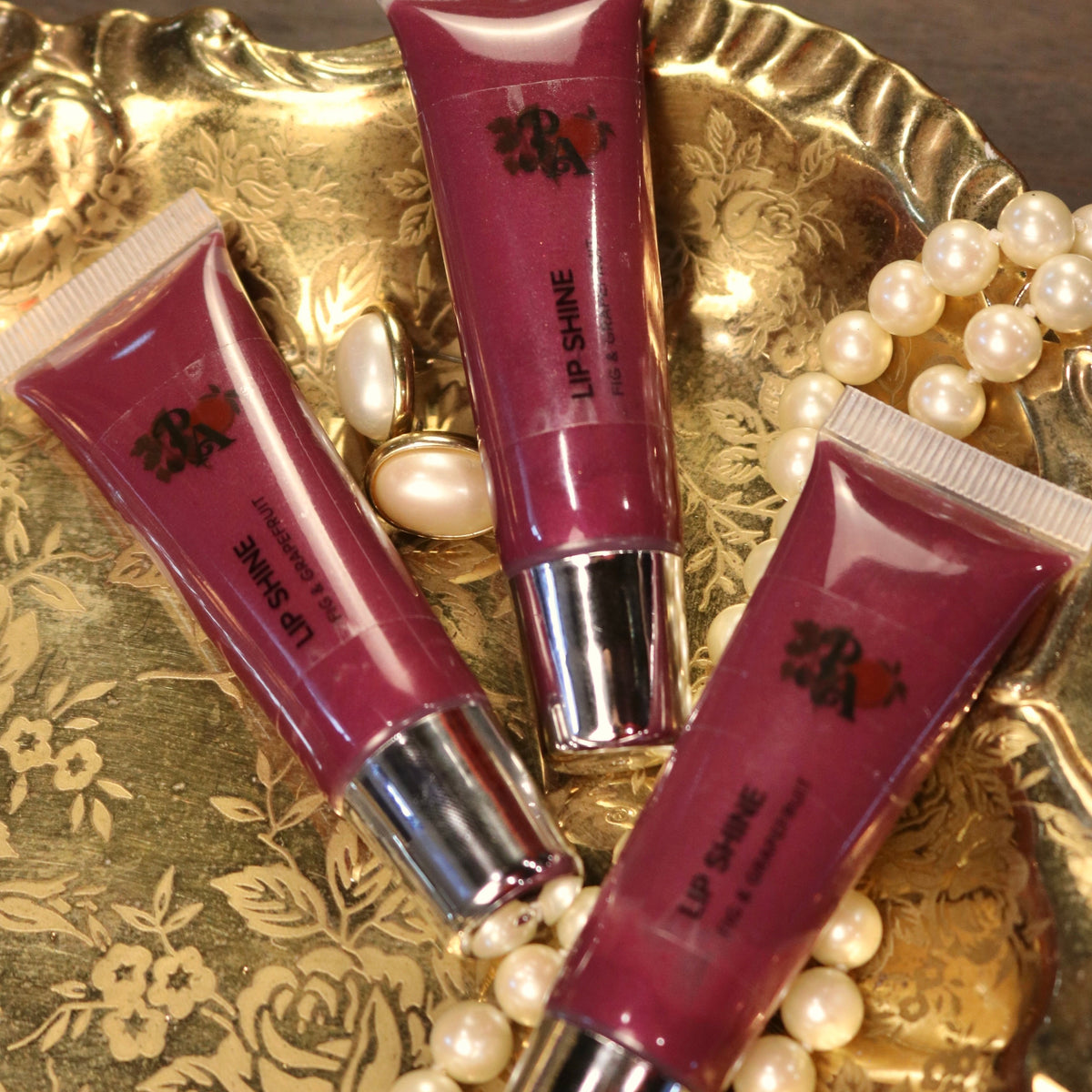 Three lip gloss tubes on a decorative gold tray with pearls