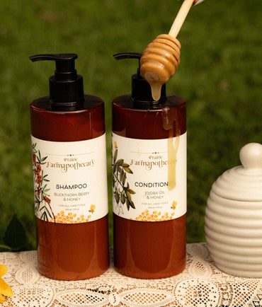 Two bottles of Farmhouse Fresh shampoo and conditioner with a honey dipper on a lace tablecloth.