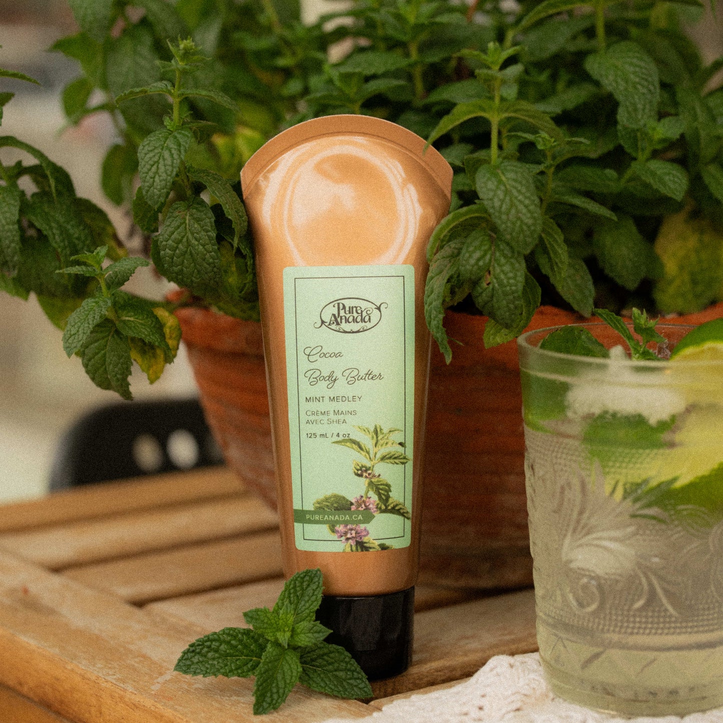 Tube of body scrub with a plant and glass in the background