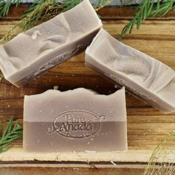 Handmade Patchouli Vanilla soap bars on a wooden surface with greenery in the background.