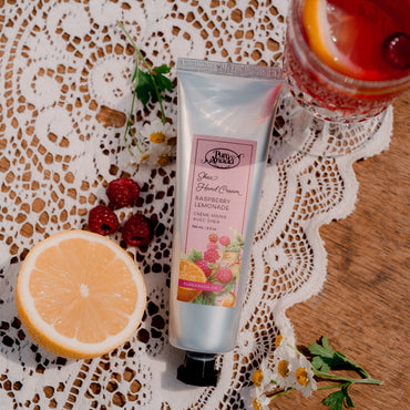 Hand cream tube with a glass of red beverage and lemon slice on a lace tablecloth
