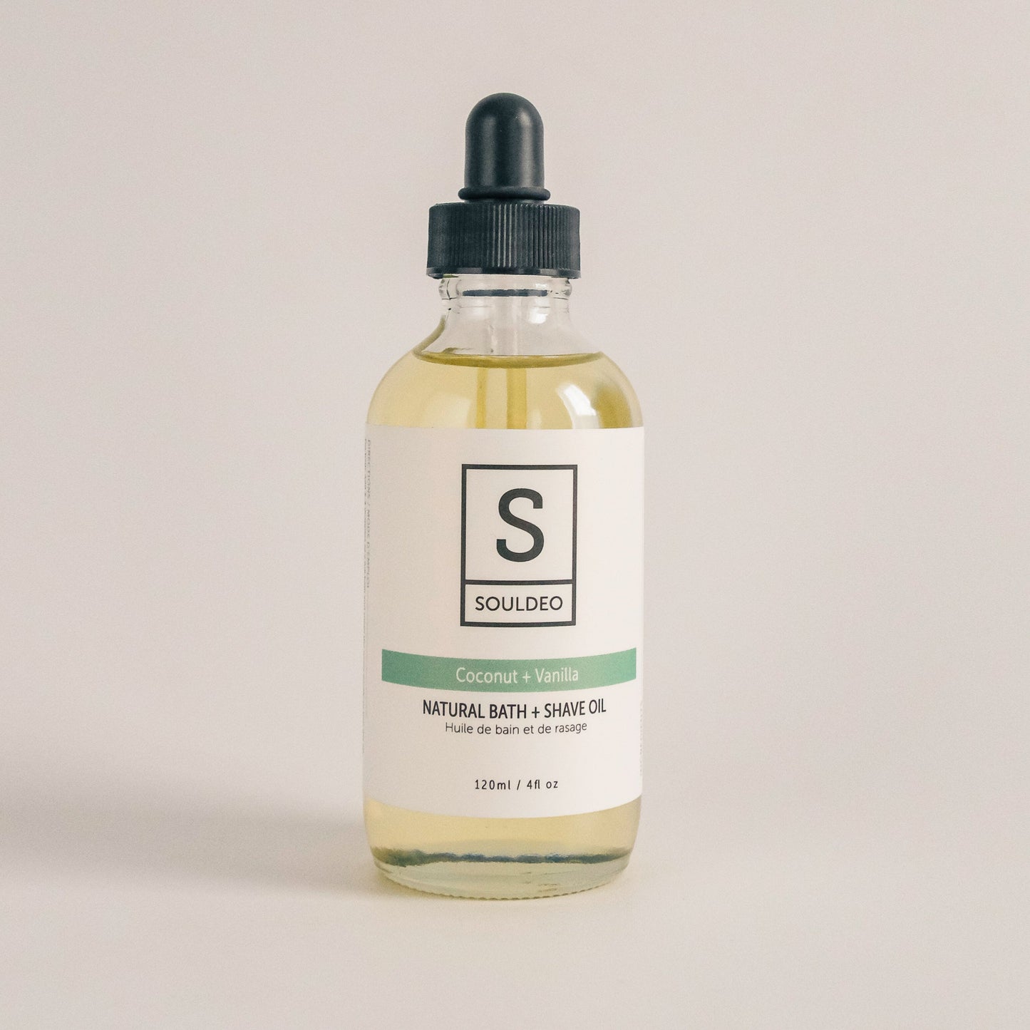 A clear glass bottle with a dropper containing yellow liquid, labeled SoulDeo Bath & Shave Oil, with a white background.