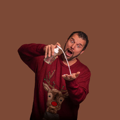 Man in a red sweater with a reindeer design pouring liquid from a bottle against a brown background