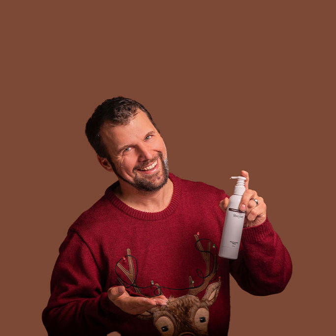 Man in red sweater holding a bottle of hand sanitizer against a brown background