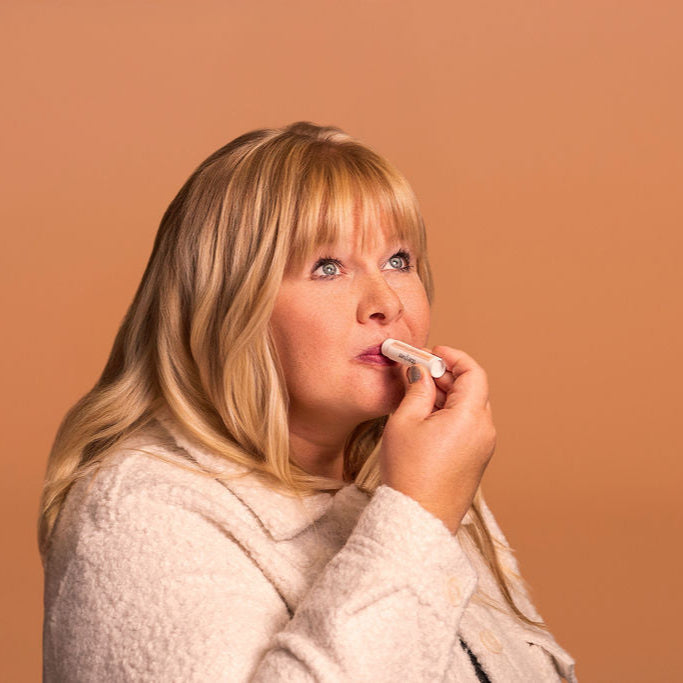 Woman applying lipstick against a brown background