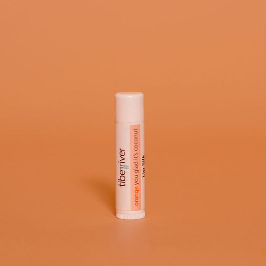 Lip balm tube labeled 'the river' on an orange background