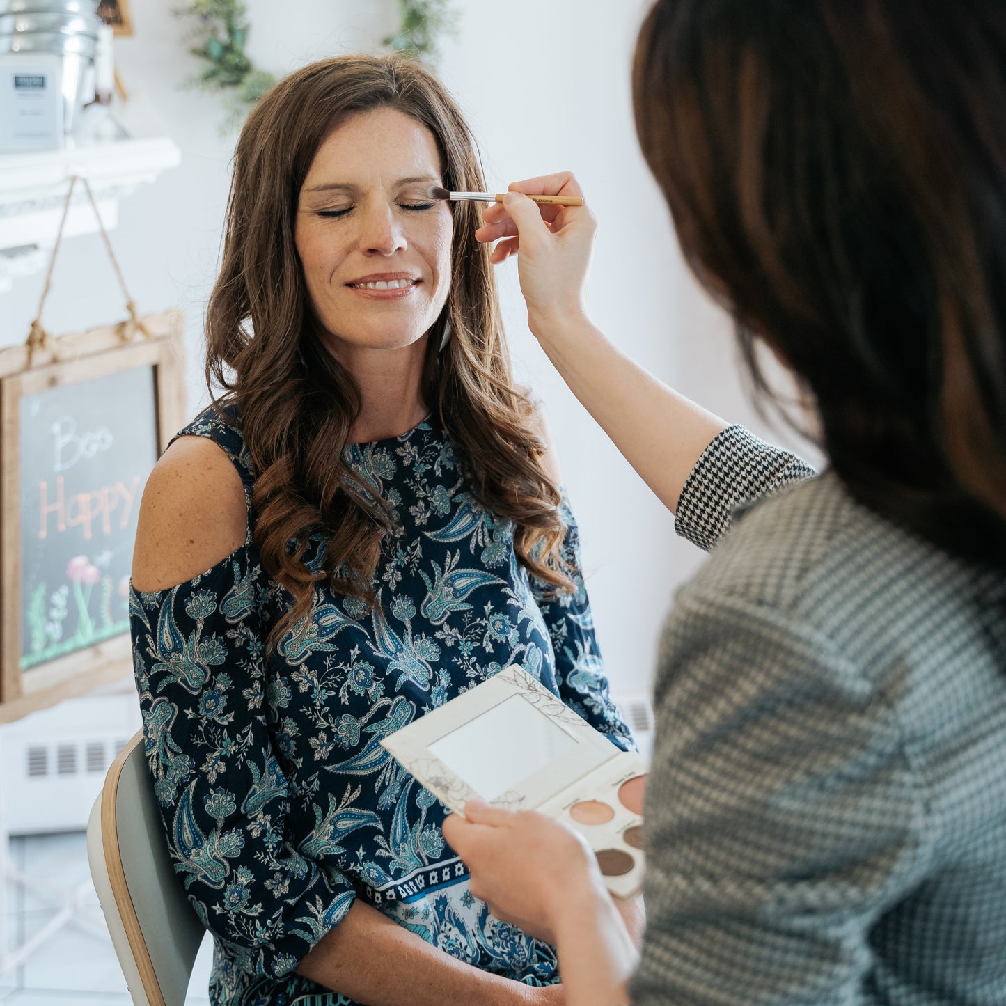 Makeup artist applying makeup to a client in a cozy room.