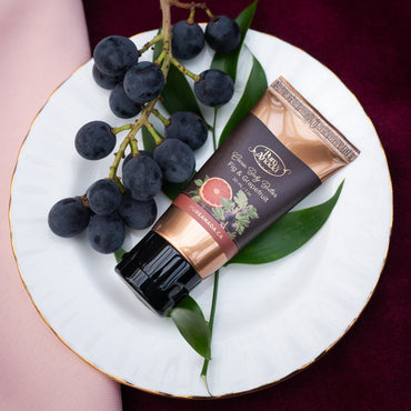 Hand cream tube with grapes on a white plate against a dark background