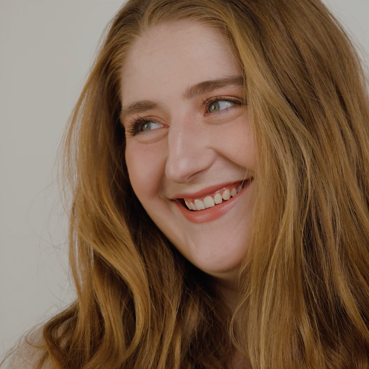 Woman with long, wavy hair smiling against a plain background